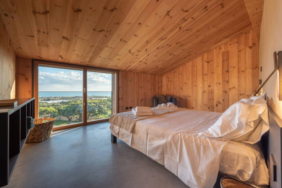The neutral materials used in the bedroom frame the panorama that can be seen through the large windows.