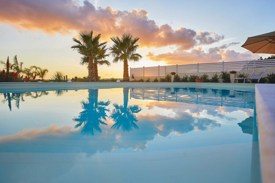 Palm trees embraced by the colours of the sunset reflected in the waters of the pool