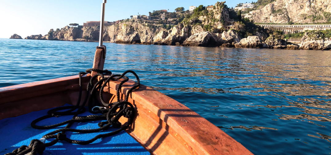 Tourist boat offering a sweeping view of the picturesque coastline near Isola Bella in Taormina, Sicily, with the tranquil turquoise Ionian Sea as backdrop.