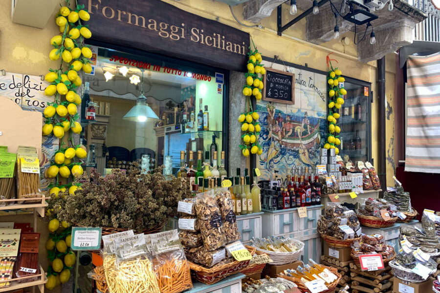 Taormina's Sicilian street shop brimming with a selection of traditional food items including regional cheeses, handmade pasta, and fresh lemons.