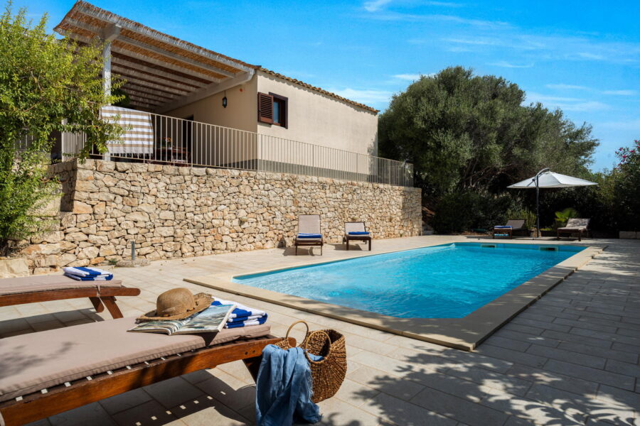 A picturesque Sicily villa surrounded by lush greenery, featuring a refreshing swimming pool.