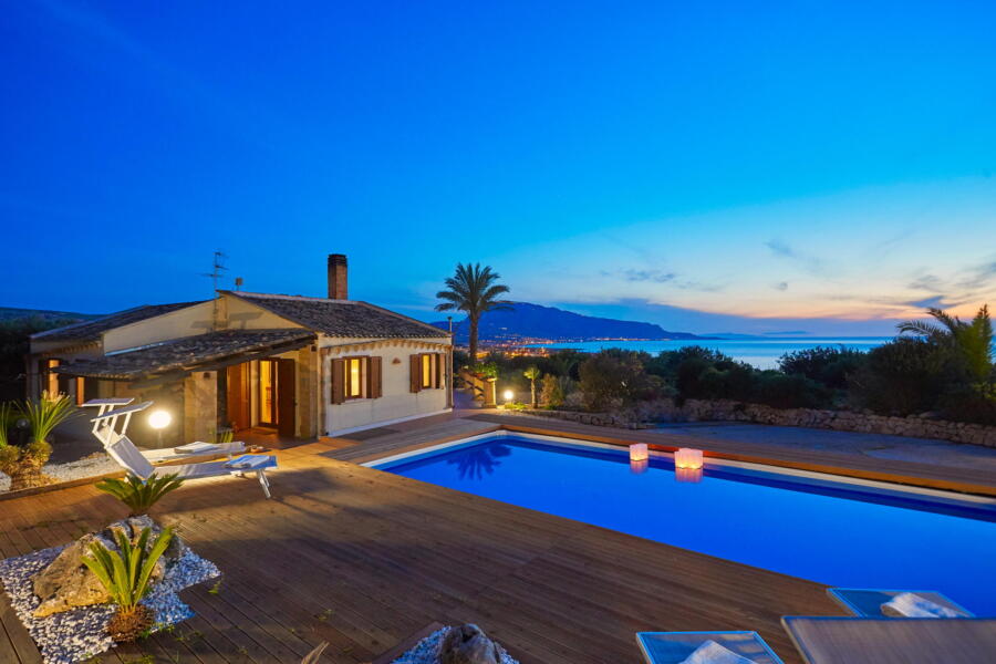 Evening view of Villa Nature's Embrace with pool lights and a coastal backdrop.