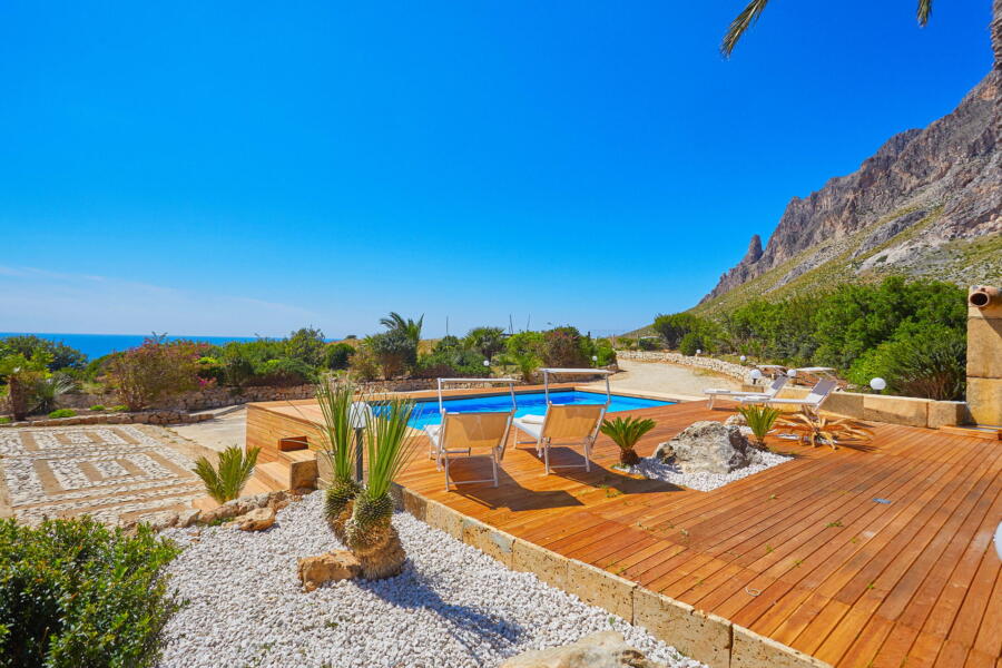 Sunny pool deck with loungers and mountain views at a Sicilian villa.