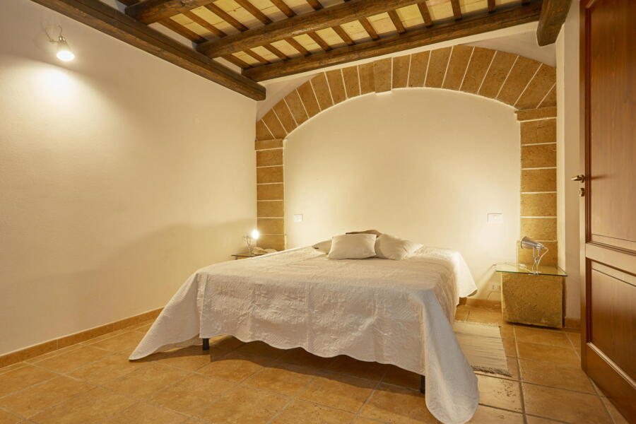 Master bedroom with terracotta tiles and exposed beams at Villa Nature's Embrace in Sicily.