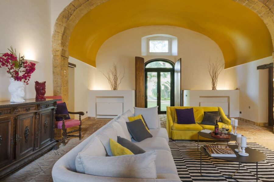 Colorful living room at Villa Selvira, a Sicily luxury villa, featuring arched stone details, bold furniture, and garden views.