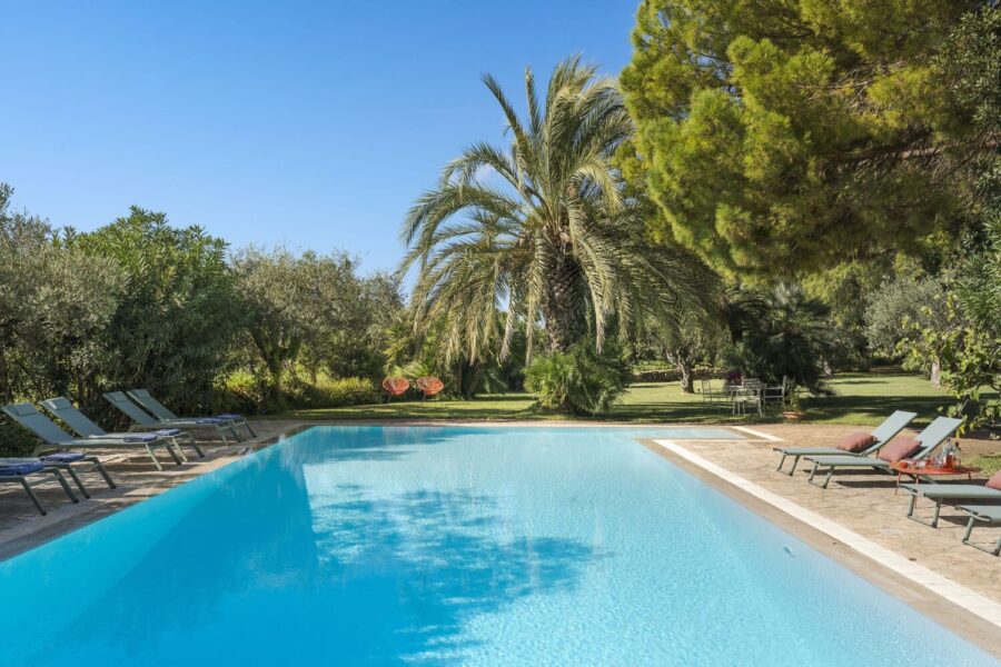 Crystal-clear pool surrounded by palm trees and sun loungers at Villa Selvira, Sicily luxury villa