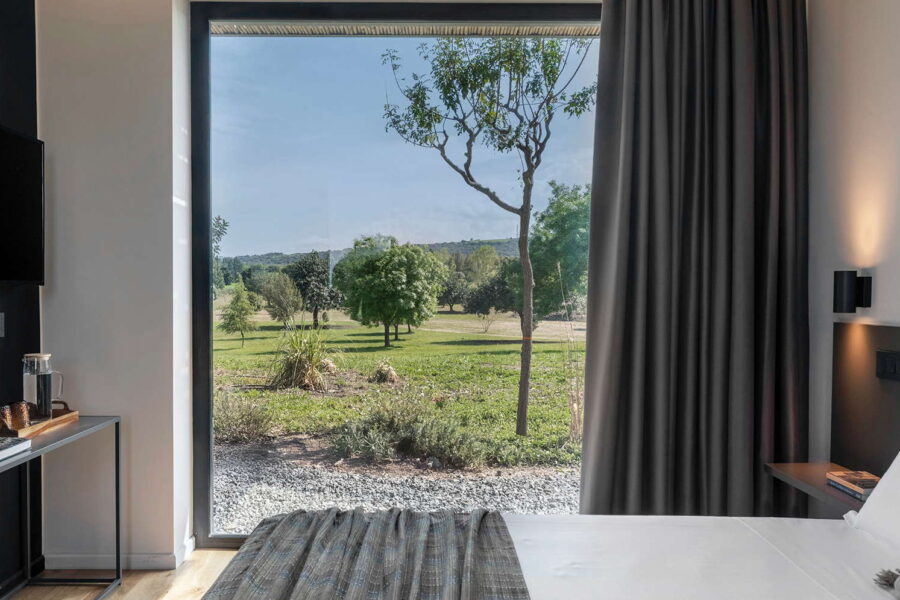 Bright bedroom interior at Nature Luxe Cottage with large window overlooking Sicilian countryside and trees.