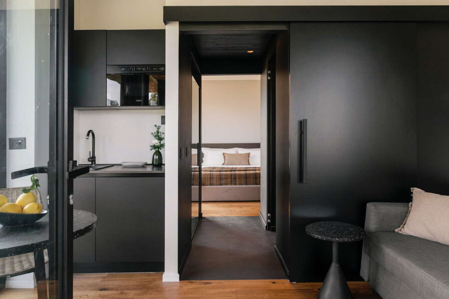 Minimalist interior with kitchenette, cozy living area, and a view into the bedroom at Nature Luxe Cottage in Sicily.