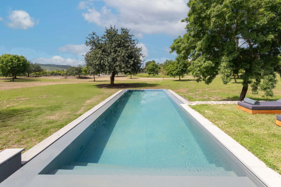 Modern rectangular pool surrounded by green fields, trees, and sun loungers at Nature Luxe Cottage, Sicily.