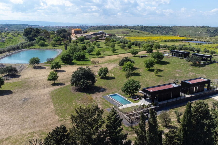 Aerial view of Nature Luxe Cottage estate with private pools, modern villas, gardens, and distant farmland in Sicily.