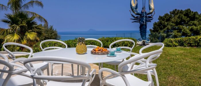 Outdoor dining terrace with sea view at Villa Orlaya in Sicily featuring modern white furniture and garden setting – Sicily villas with pool by Scent of Sicily