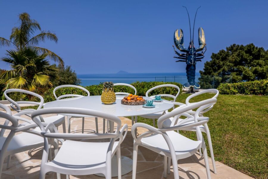 VillaOrlaya-Capo-di-Orlando-DinningOutiside-ScentOfSicily Outdoor dining terrace with sea view at Villa Orlaya in Sicily featuring modern white furniture and garden setting – Sicily villas with pool by Scent of Sicily