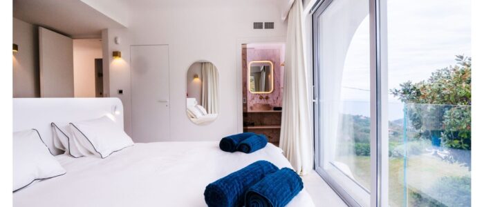 Bright bedroom suite with panoramic windows and en suite bathroom at Villa Orlaya, a luxury Sicily villa with pool and contemporary coastal interiors.