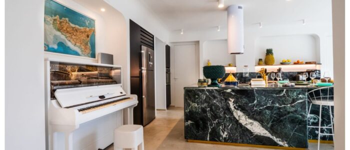 Modern kitchen and piano corner at Villa Orlaya, a stylish Sicily villa with pool featuring marble interiors, contemporary décor, and elegant open-plan living spaces.