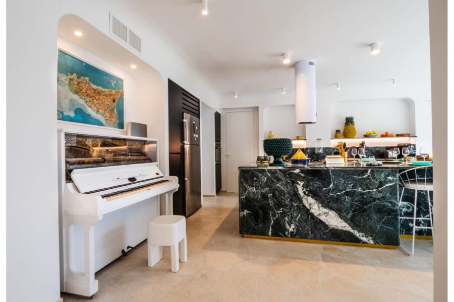 VillaOrlaya-Capo-di-Orlando-PianoCorner-ScentOfSicily Modern kitchen and piano corner at Villa Orlaya, a stylish Sicily villa with pool featuring marble interiors, contemporary décor, and elegant open-plan living spaces.