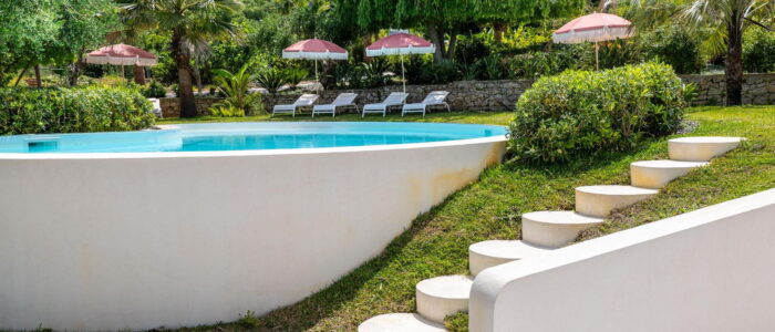 VillaOrlaya-Capo-di-Orlando-ToPatio-ScentOfSicily Villa Orlaya garden and swimming pool with palm trees, sun loungers, and Mediterranean greenery in Sicily, Sicily villas with pool by Scent of Sicily